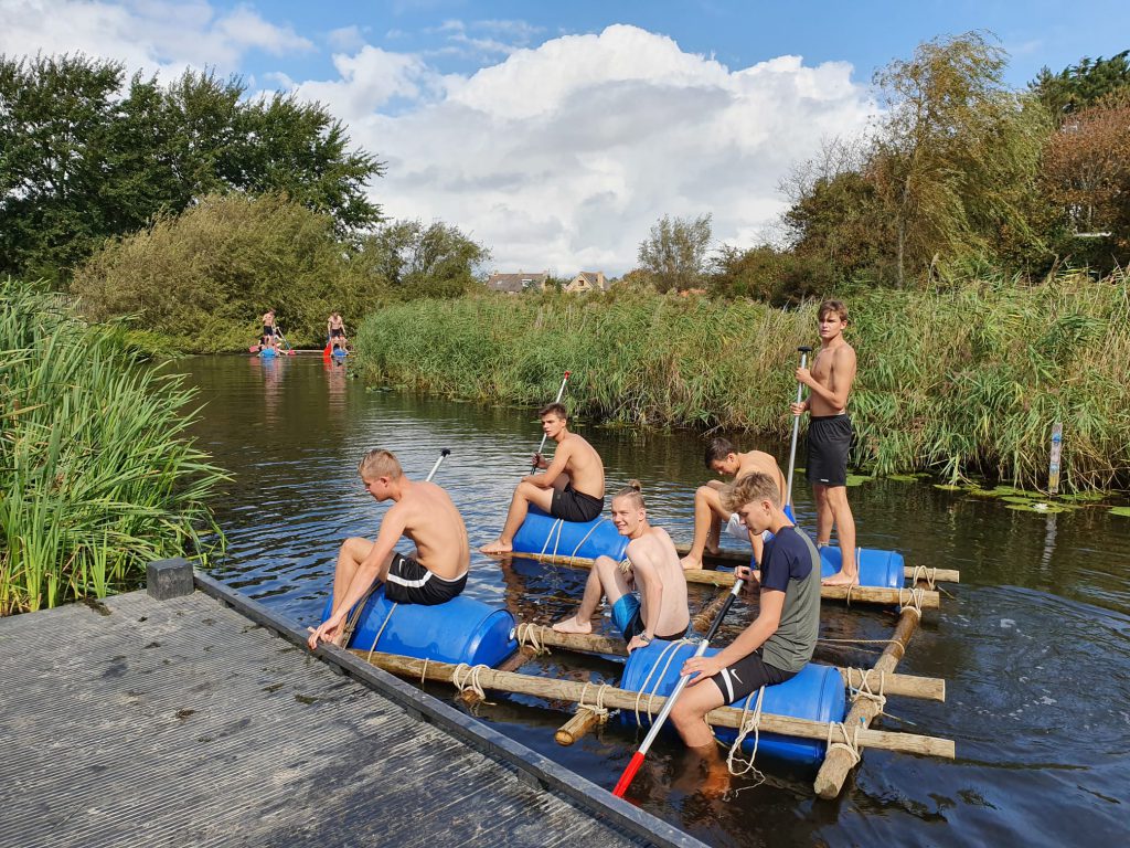 Jongens hebben zelf een vlot gebouwd van touwen, tonnen en balken bij Kanoverhuur Den Helder